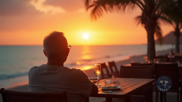 Mature solo traveller over 50 enjoying a quiet beachfront dinner at sunset, with a glass of wine and a golden sky setting the scene—perfect for a light and relaxing first day after a long-haul flight.