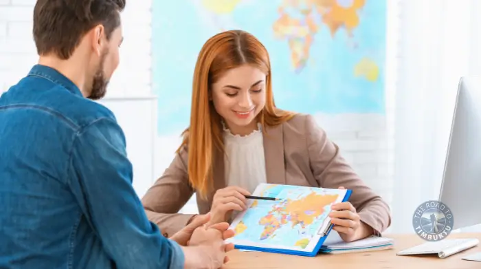 Travel agent helping a client plan a tailor-made holiday using a world map—perfect for crafting spontaneous getaways for solo travellers over 50 who know exactly what they want (and when).