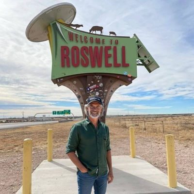 Is It Safe to Travel to the USA Solo Over 50? A mature solo traveller standing beside the ‘Welcome to Roswell’ sign in New Mexico, enjoying a quirky stop on a U.S. road trip